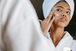 Woman in a bathrobe practices her skincare routine with moisturizing cream. Perfect for wellness themes.